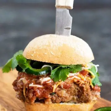 a meatloaf burger on a cutting board with a knife stabbing into it