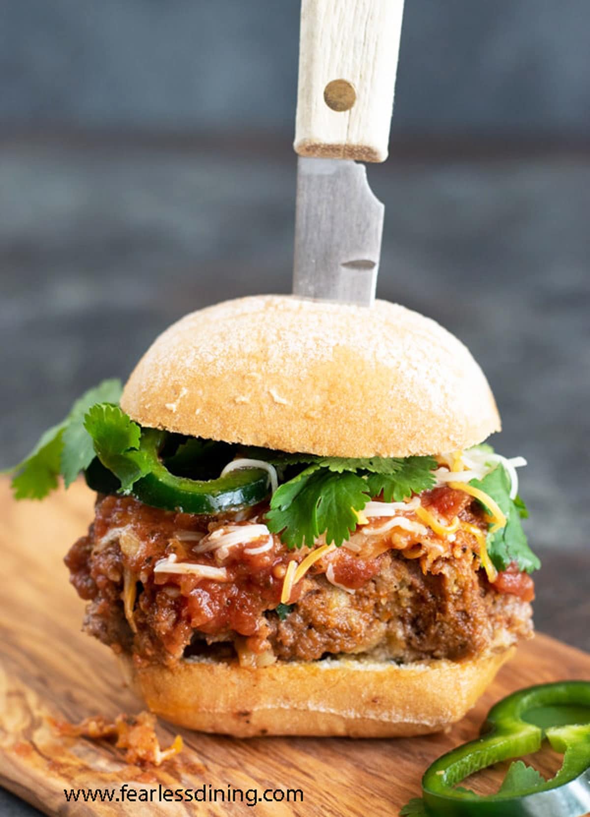 A taco meatloaf burger on a cutting board with a knife stabbing into it.