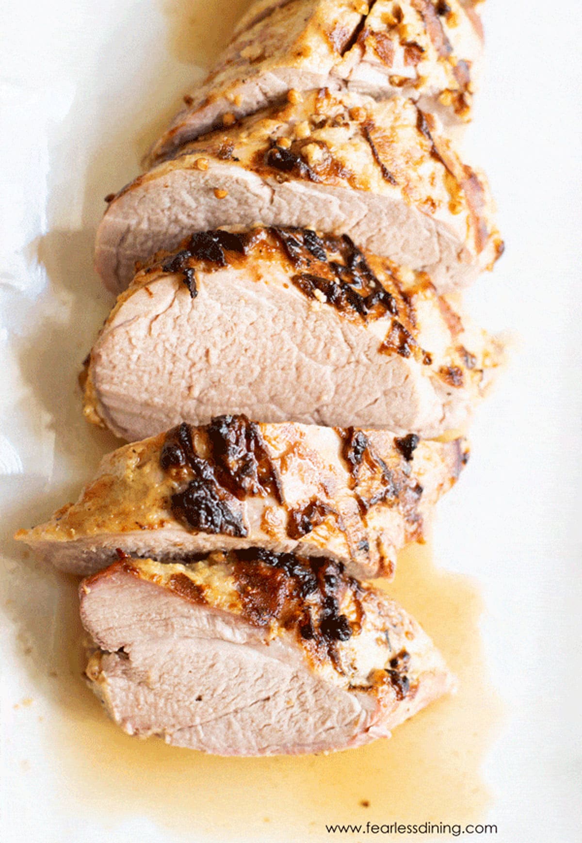 A sliced pork tenderloin on a white plastic cutting board.