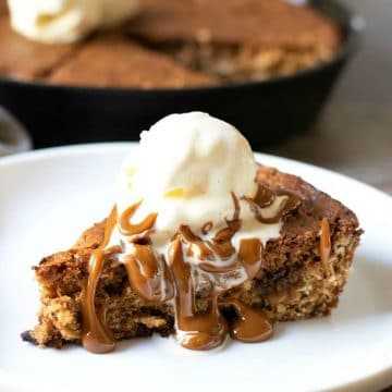 a slice of skillet cookie on a plate. It is topped with a scoop of ice cream and hot caramel.