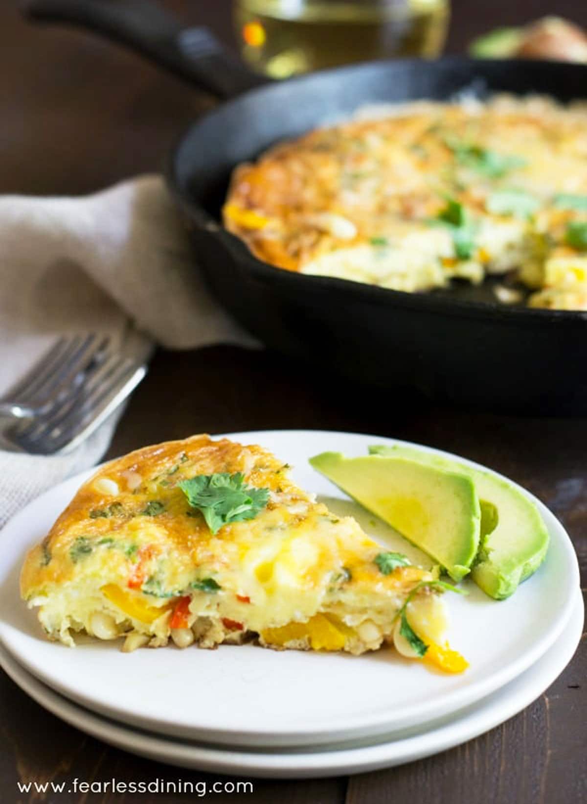 A slice of frittata on a plate with avocado slices.