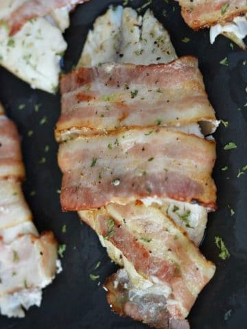cooked tilapia wrapped in bacon on a baking sheet
