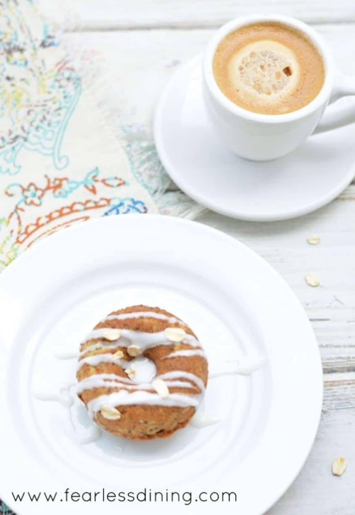 A donut on a white plate next to an espresso.