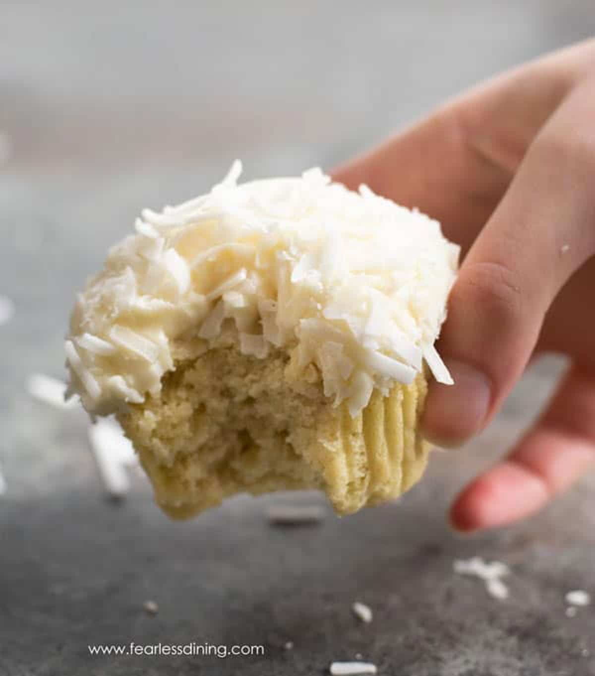 A hand holding a cupcake with a bite taken out.
