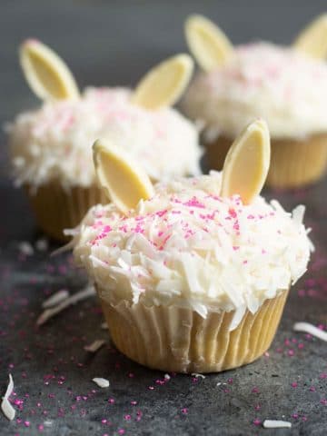 Coconut cupcakes decorated with white chocolate bunny ears for Easter.