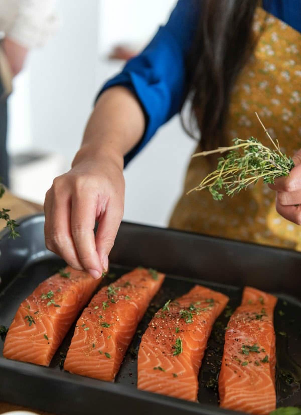 A hand dropping fresh herbs on raw salmon.