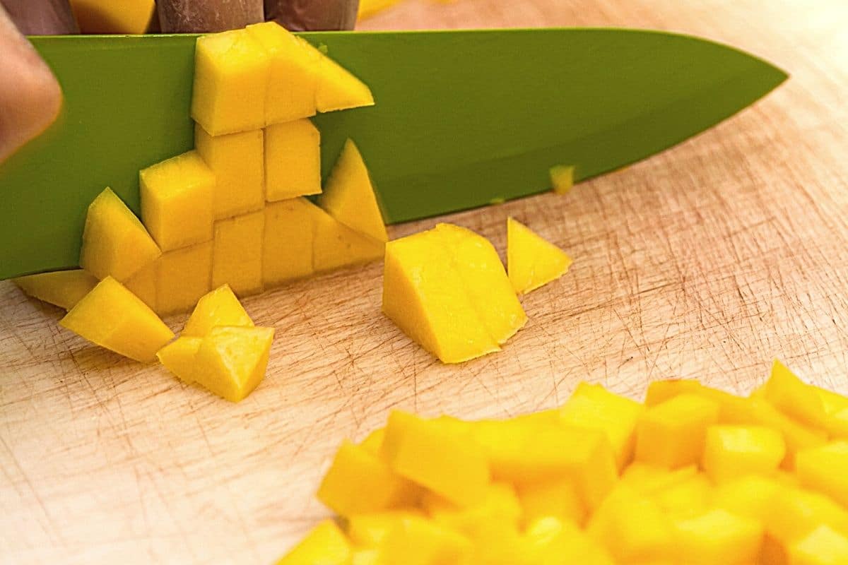 Cutting mango on a wooden cutting board.