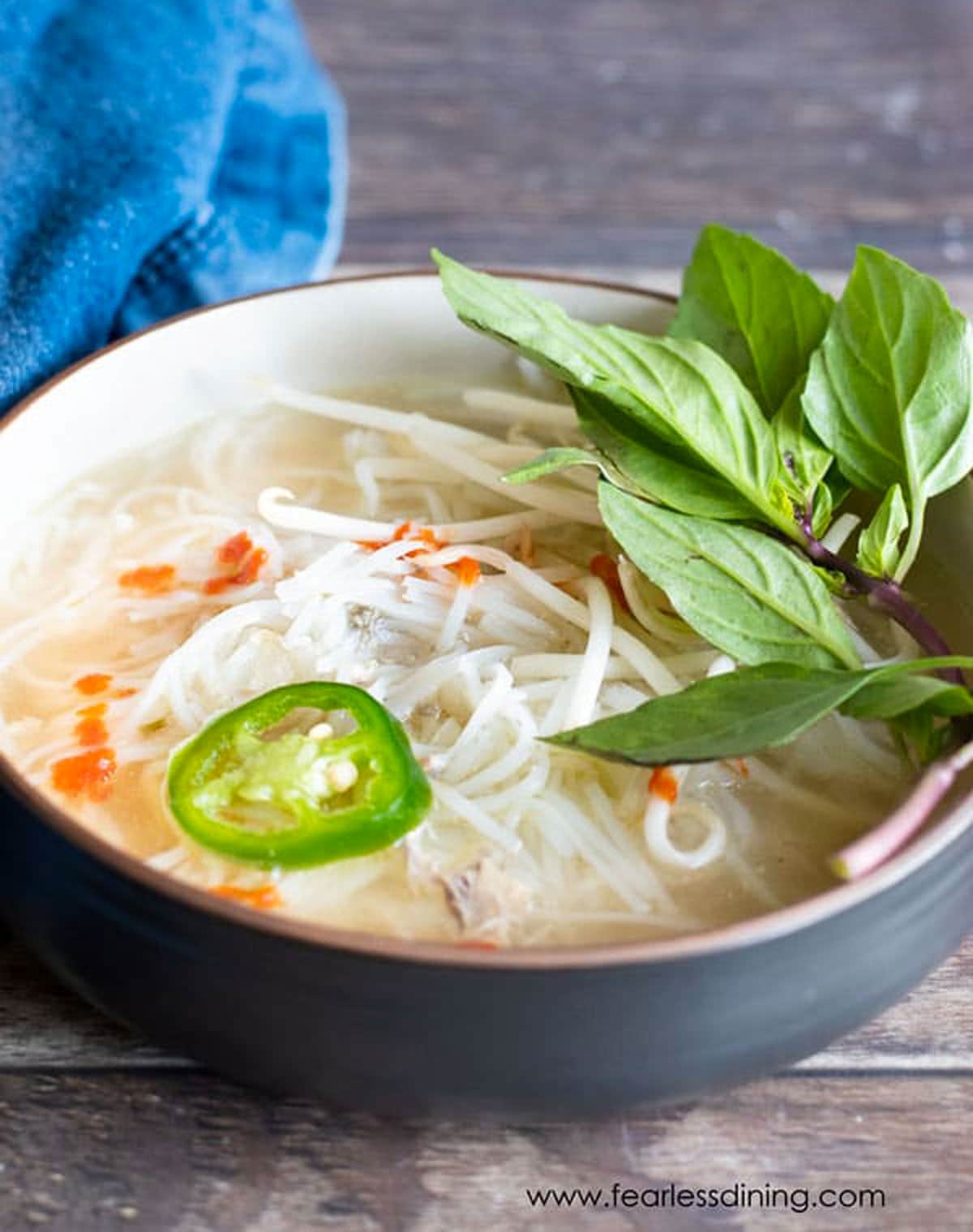 A bowl of pho topped with basil and jalapeño.