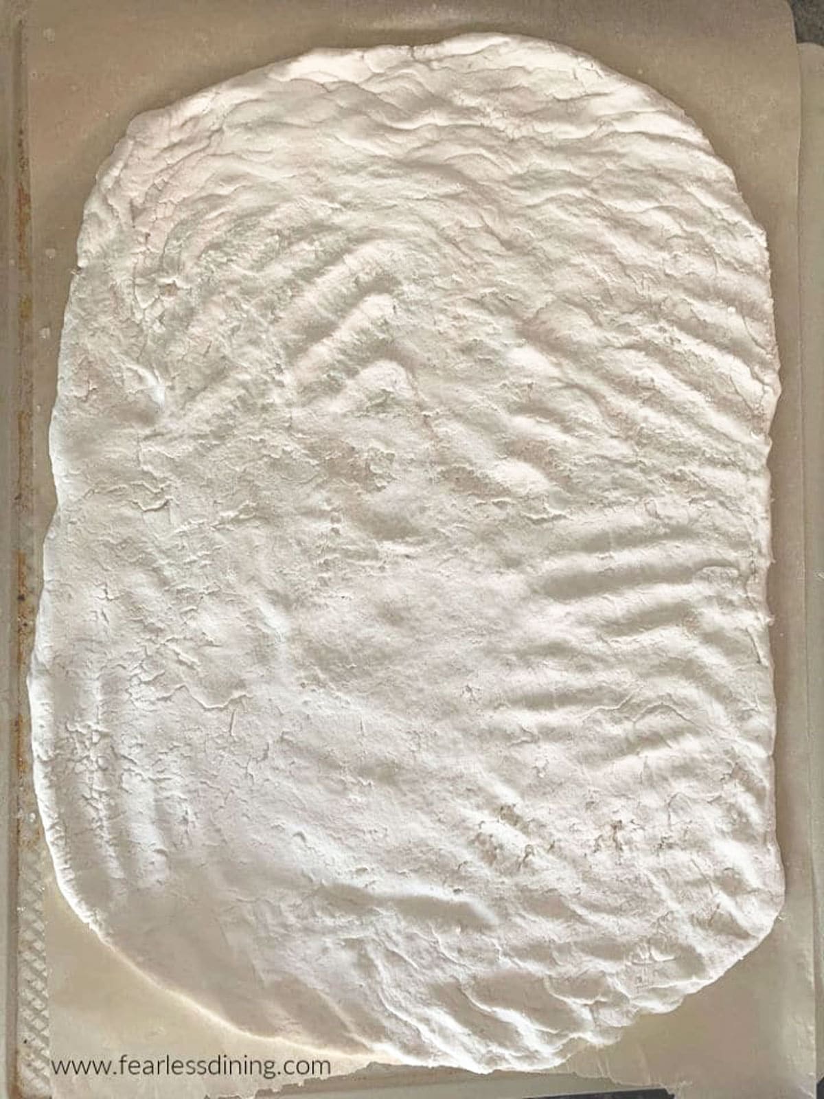 An unbaked pizza crust on a baking sheet.