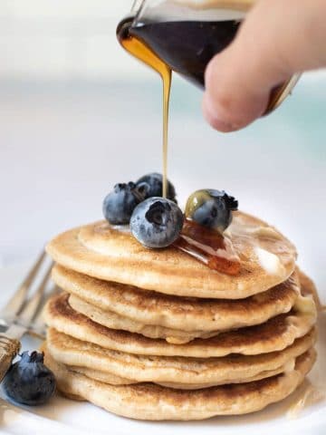 pouring syrup over a stack of gluten free pancakes