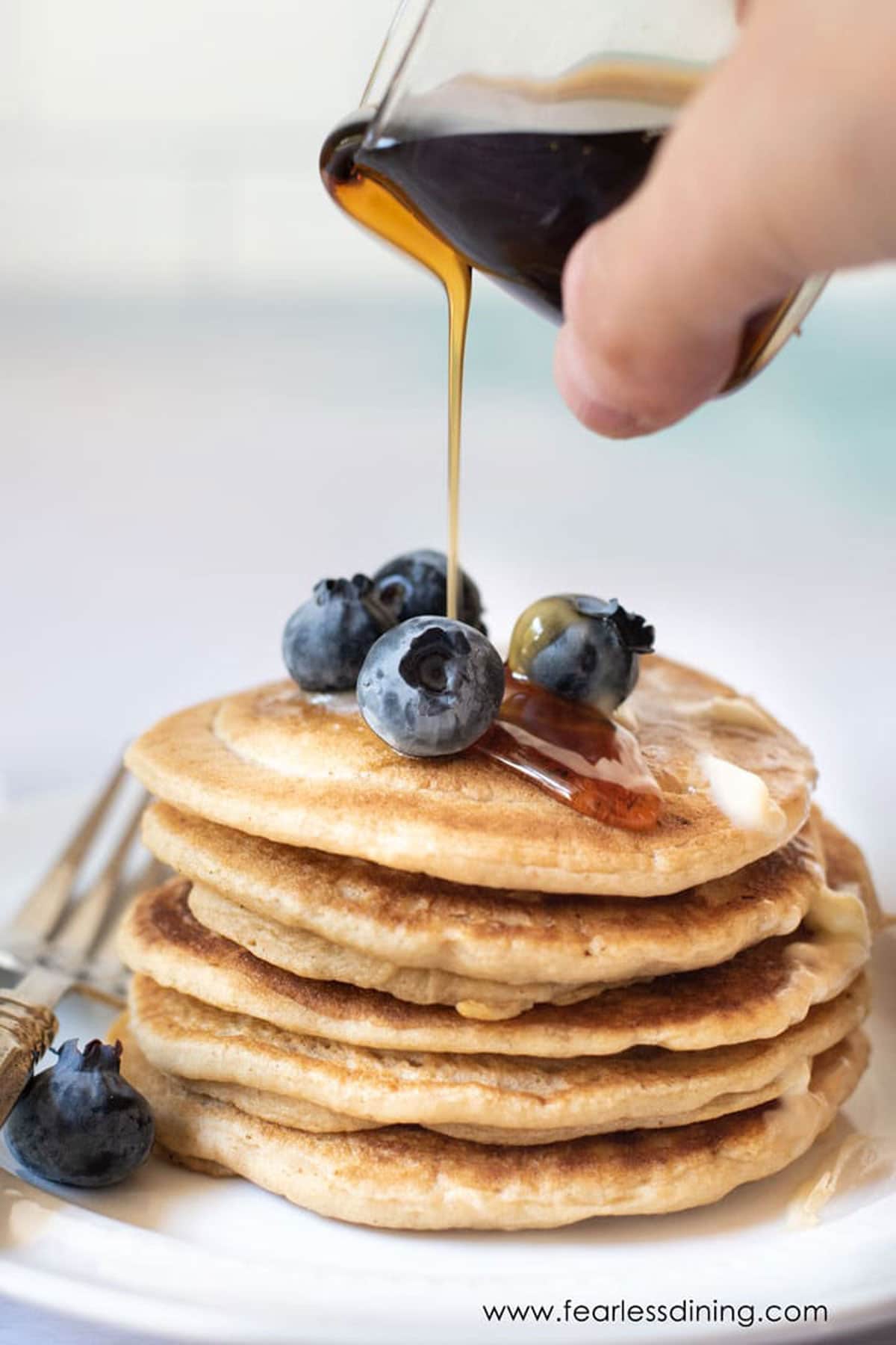Pouring syrup over a stack of gluten free pancakes.