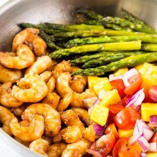 A pan filled with honey garlic shrimp, asparagus, and mango salsa.