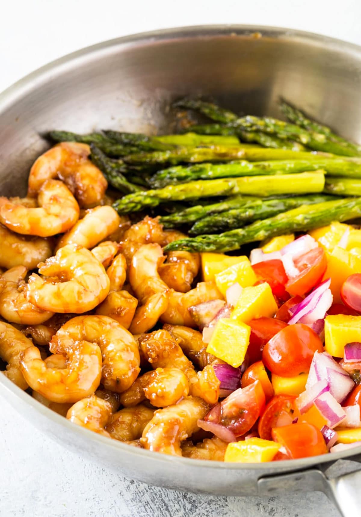 A pan filled with honey garlic shrimp, asparagus, and mango salsa.