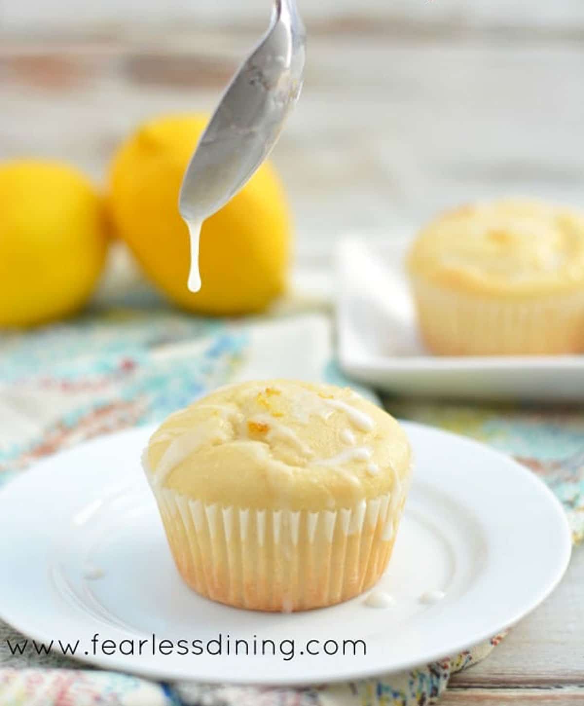 A spoon drizzling icing over a cupcake.