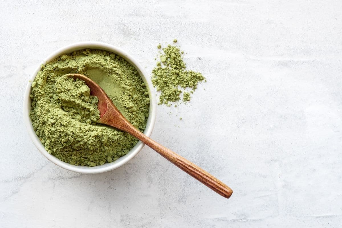 Matcha powder in a white bowl with a wooden spoon.