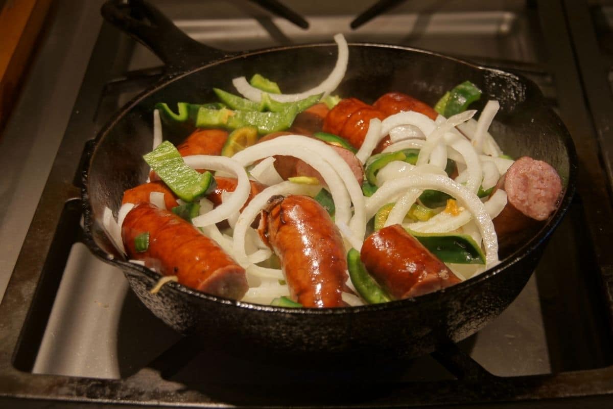 The sausage, onion, pepper cooking in a cast iron pan.
