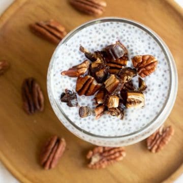 A close up view of a glass of chia pudding topped with dates and pecans