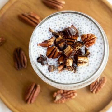 A close up view of a glass of chia pudding topped with dates and pecans.