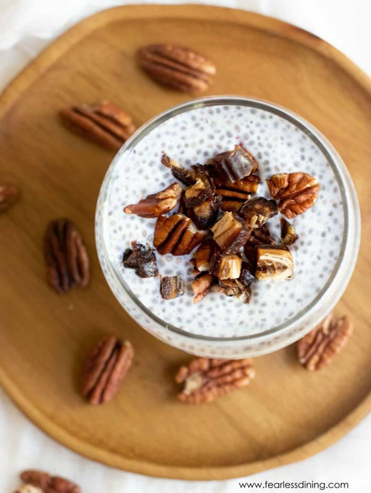 A close up view of a glass of chia pudding topped with dates and pecans.