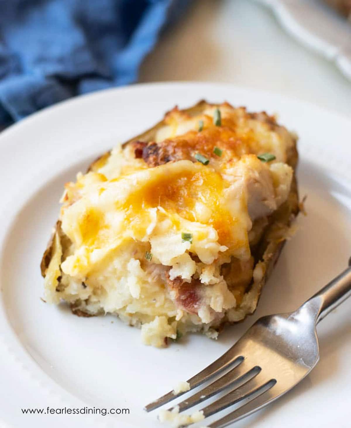 A twice baked potato on a white plate. A bite is missing from the potato.