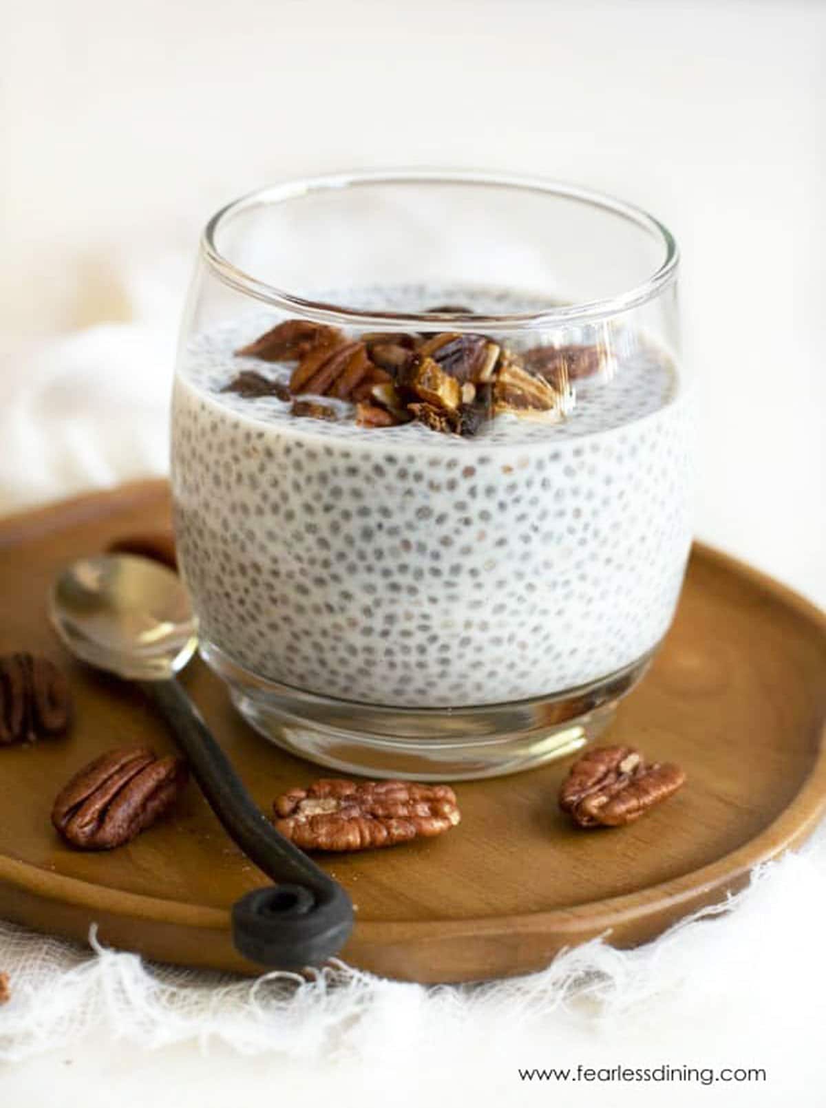A glass full of chia pudding. The glass is on a small wooden plate.