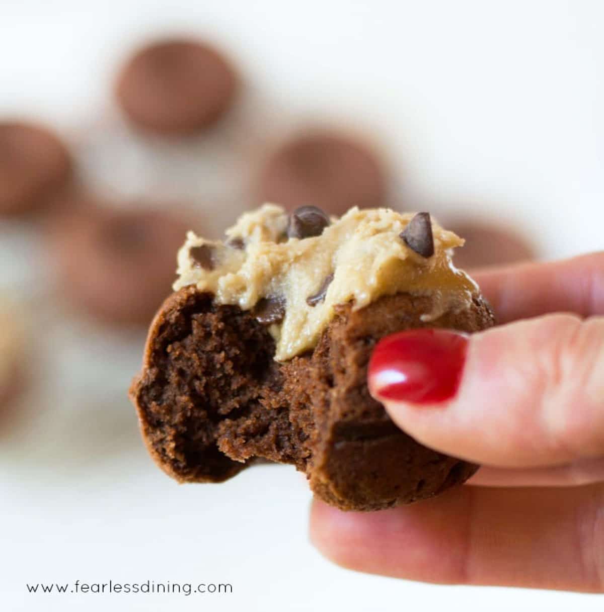 A gluten free chocolate donut with cookie dough frosting with a bite taken out.