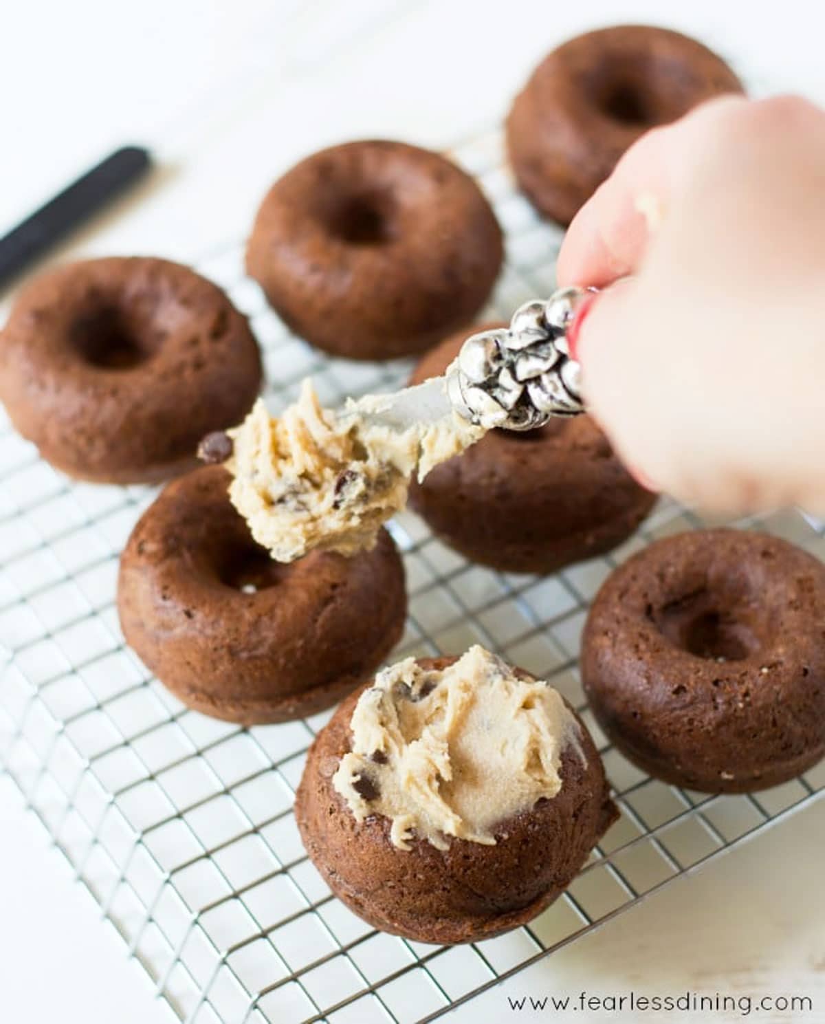 Spreading cookie dough frosting on mini chocolate donuts.
