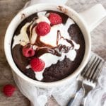 The top view of a chocolate mug cake in the mug topped with ice cream and raspberries.