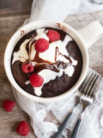 The top view of a chocolate mug cake in the mug topped with ice cream and raspberries