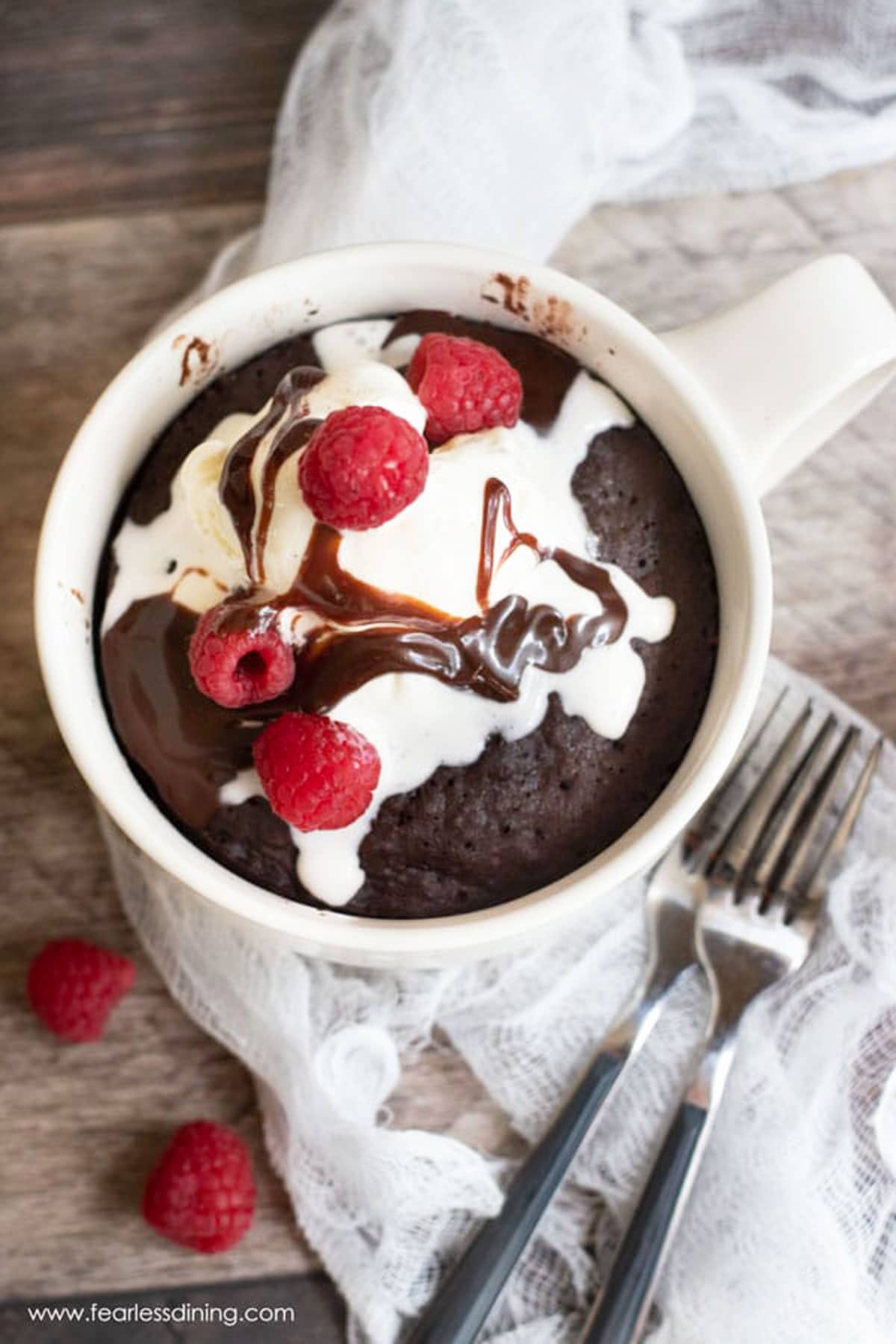 the top view of a chocolate mug cake in the mug topped with ice cream and raspberries