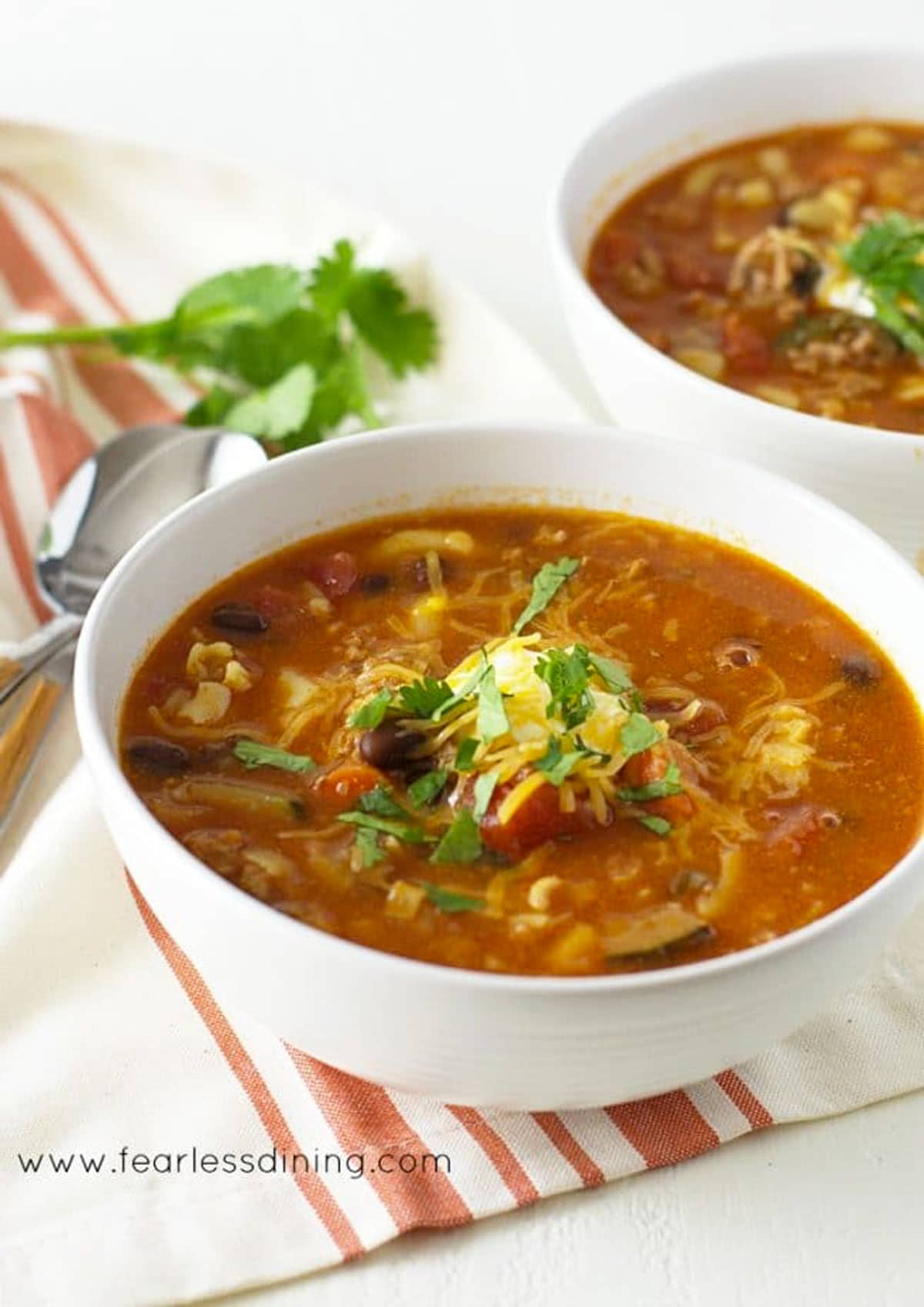 Two white bowls filled with ground pork soup. They are garnished with sour cream and cilantro.