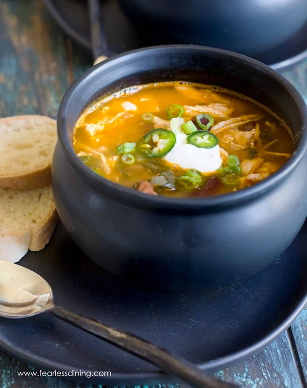 A black bowl filled with Mexican chicken soup. It is garnished with sour cream and jalapenos.