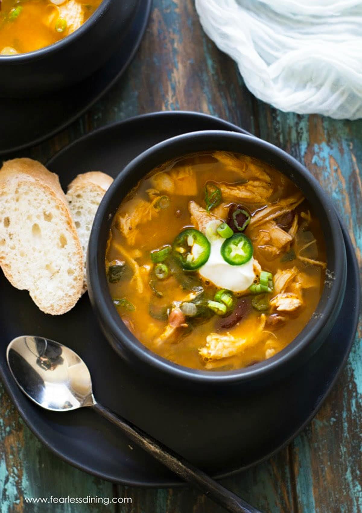 The top view of a bowl of Mexican chicken soup. There are two slices of gluten free baguettes.