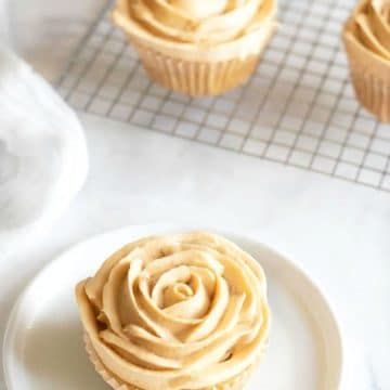 A gluten free caramel cupcake with frosting piped like flower petals on a plate.