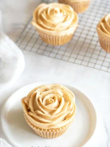 a caramel cupcake with frosting piped like flower petals on a plate