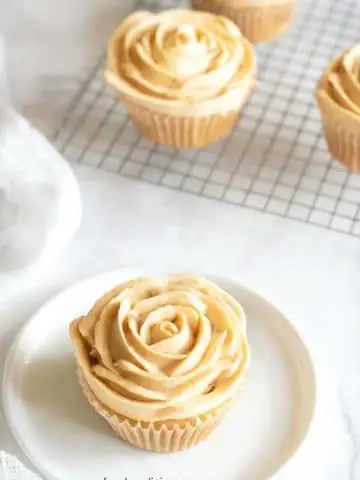 a caramel cupcake with frosting piped like flower petals on a plate