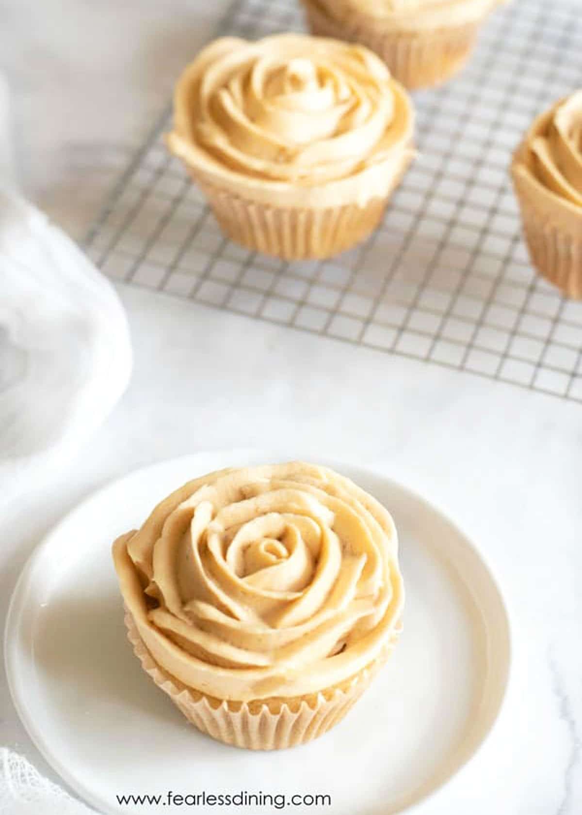 A gluten free caramel cupcake with frosting piped like flower petals on a plate.