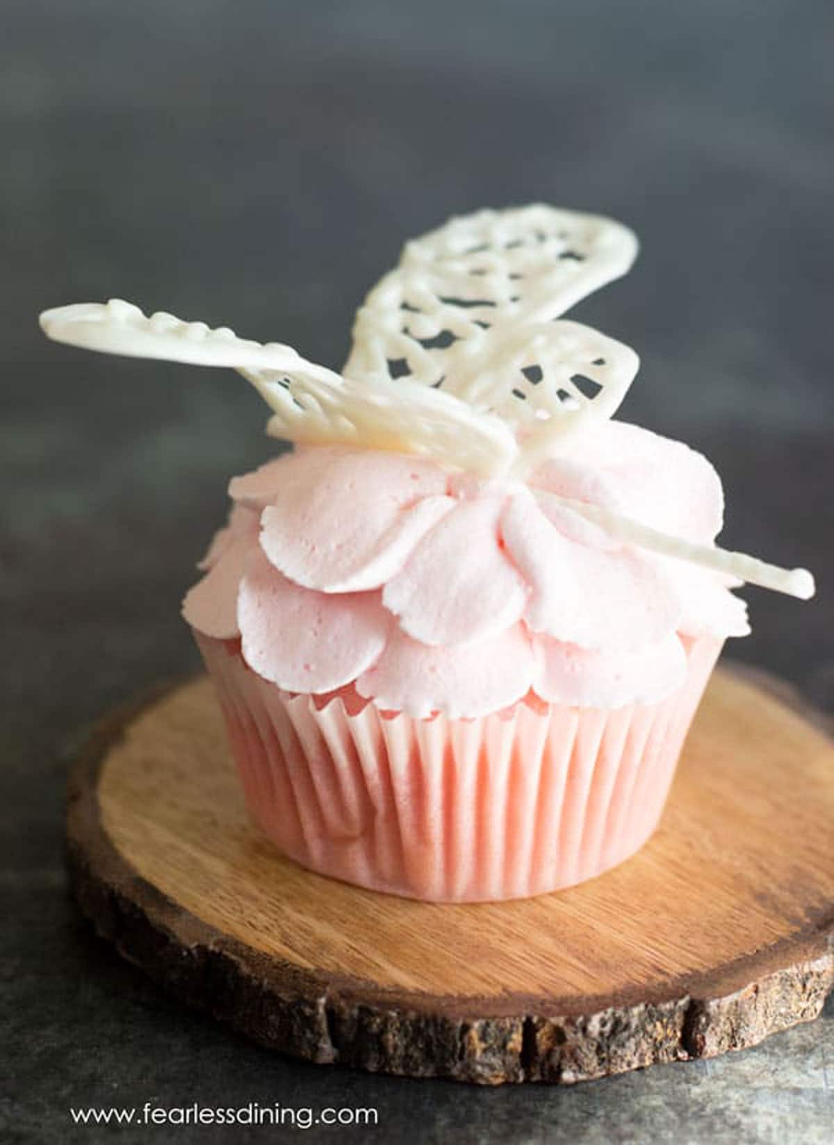 A pink lemonade cupcake on a wooden coaster.