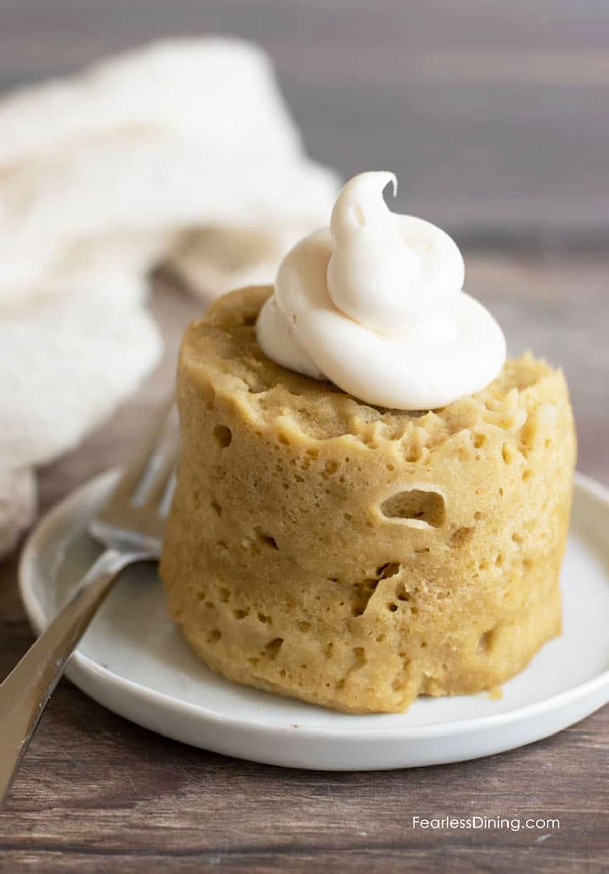 A frosted gluten free banana mug cake on a small white plate.