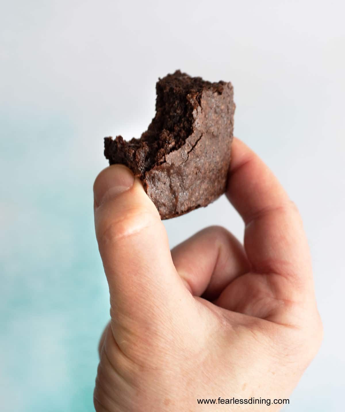 A hand holding up a brownie with a bite taken out.