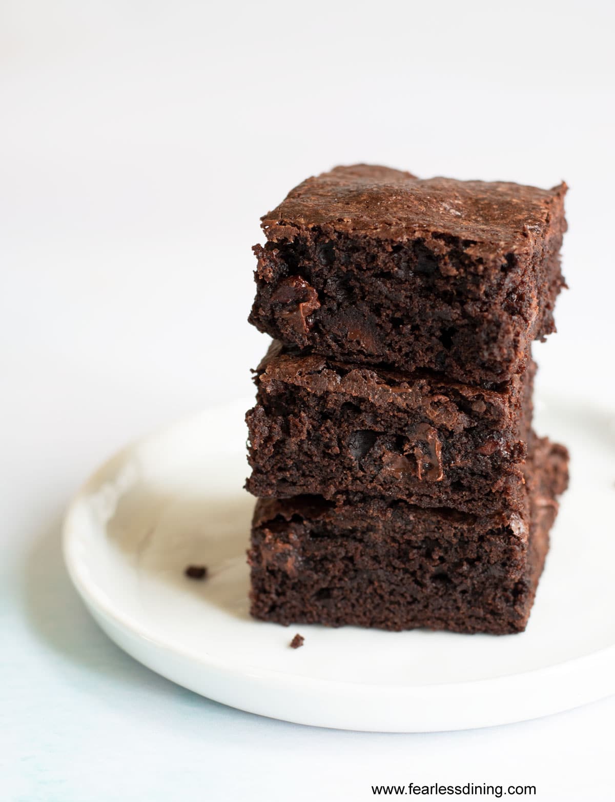 A stack of three fudgy brownies on a white plate.