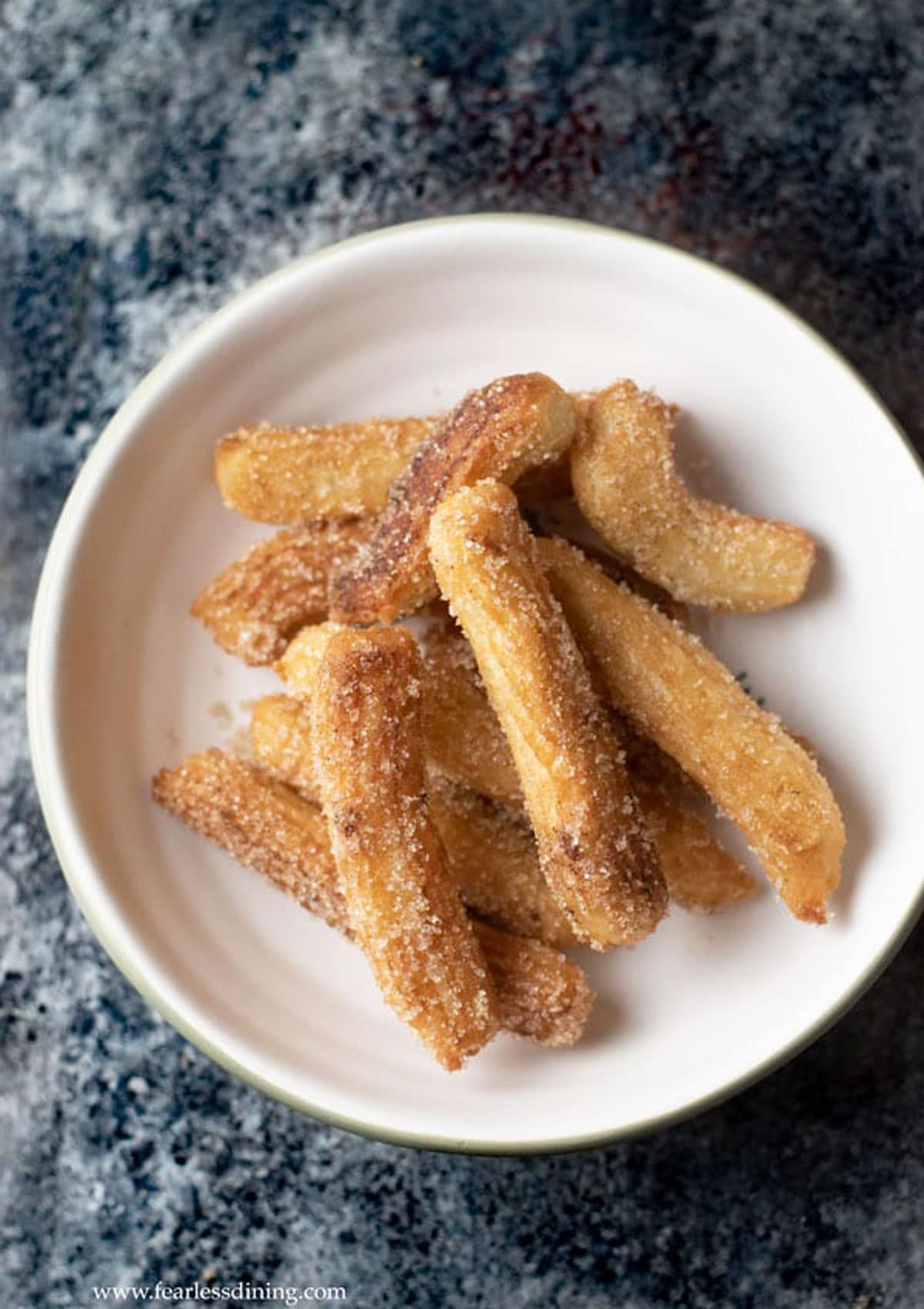 A serving bowl full of cinnamon sugar coated fried gluten free churros.