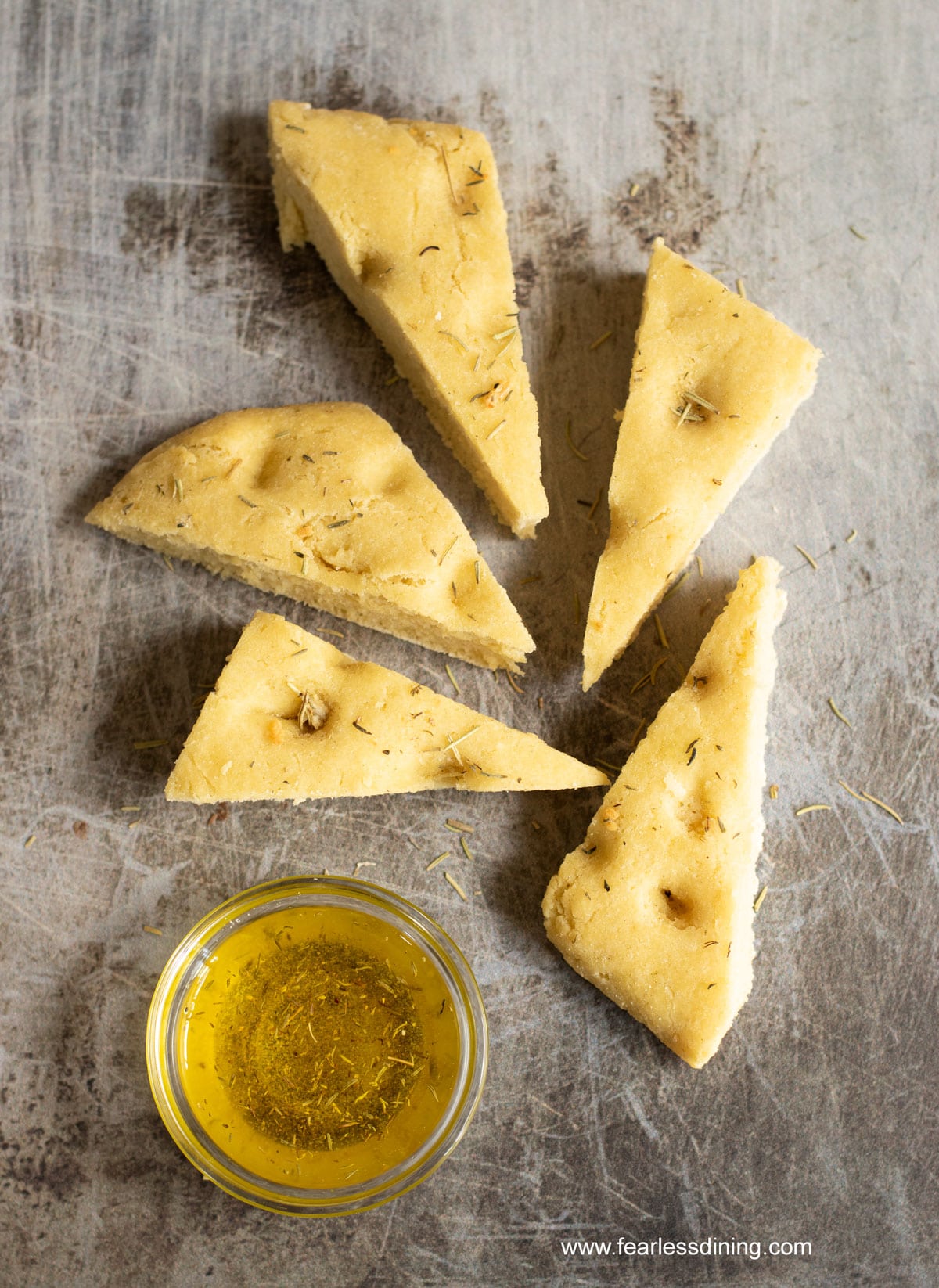 wedge shaped pieces of gluten free focaccia next to a dipping oil bowl