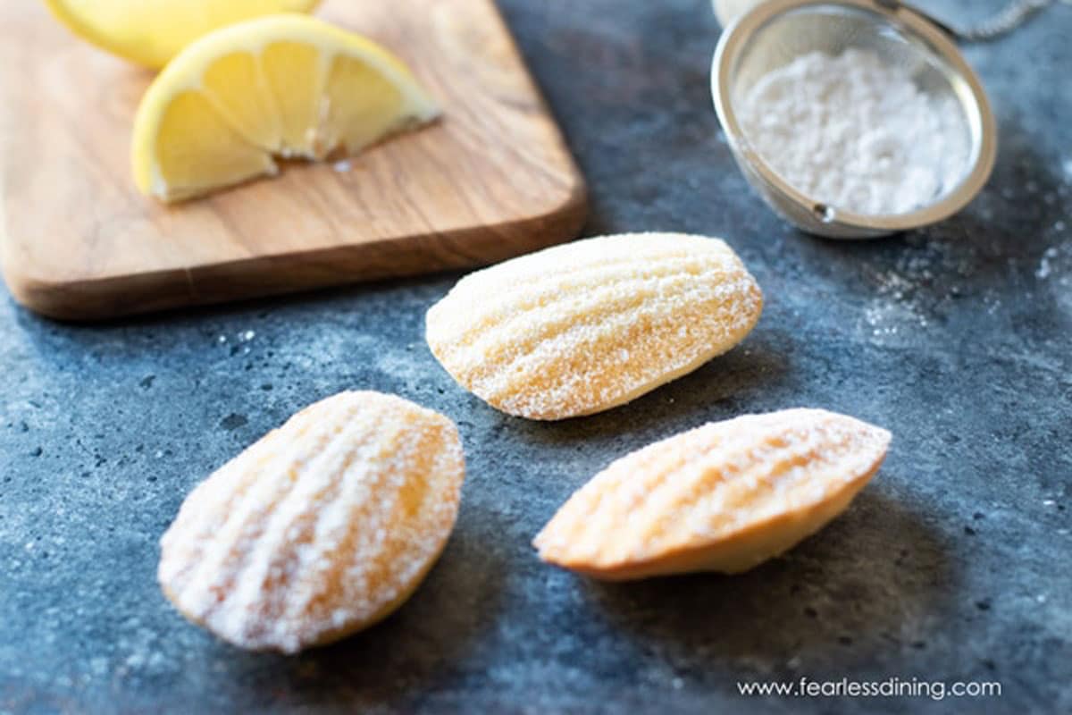 Three madeleines on the counter next to a cutting board with lemons.