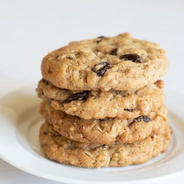 A stack of four oatmeal raisin cookies on a plate.