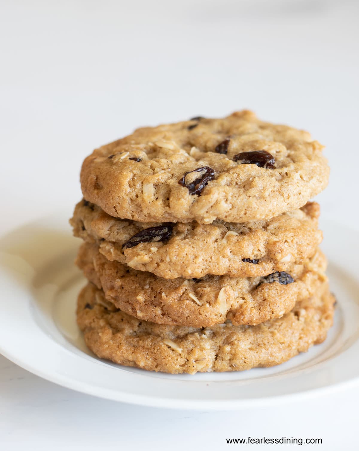 A stack of four oatmeal raisin cookies on a plate.