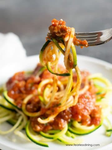 A fork holding up zucchini noodles and ground pork pasta sauce.
