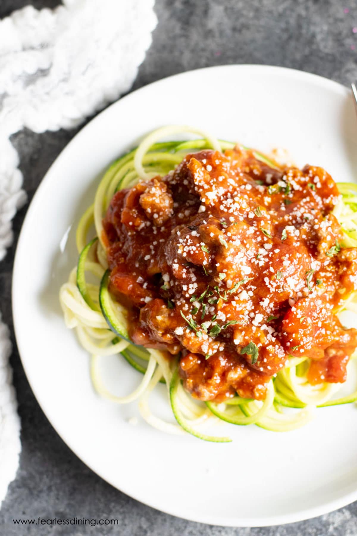 The top view of a plate of zucchini noodles topped with sauce.