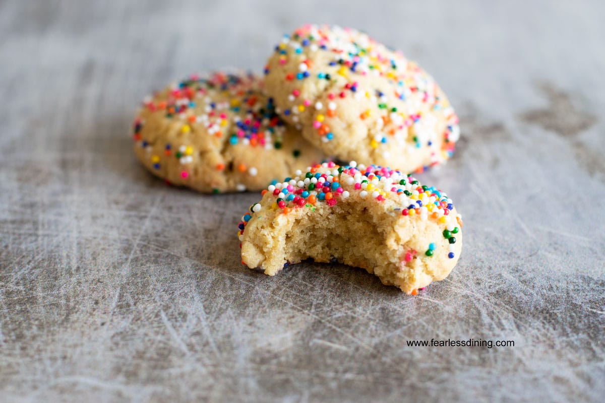 A sprinkle cookies on a cookie sheet. One has a bite taken out.