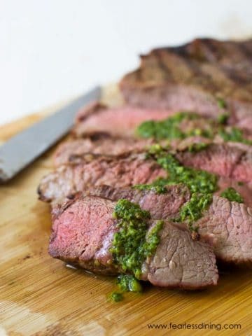 A photo of sliced steak topped in pesto sauce.